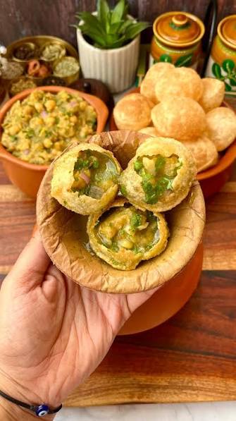A hand holding a bowl of freshly filled pani puri.